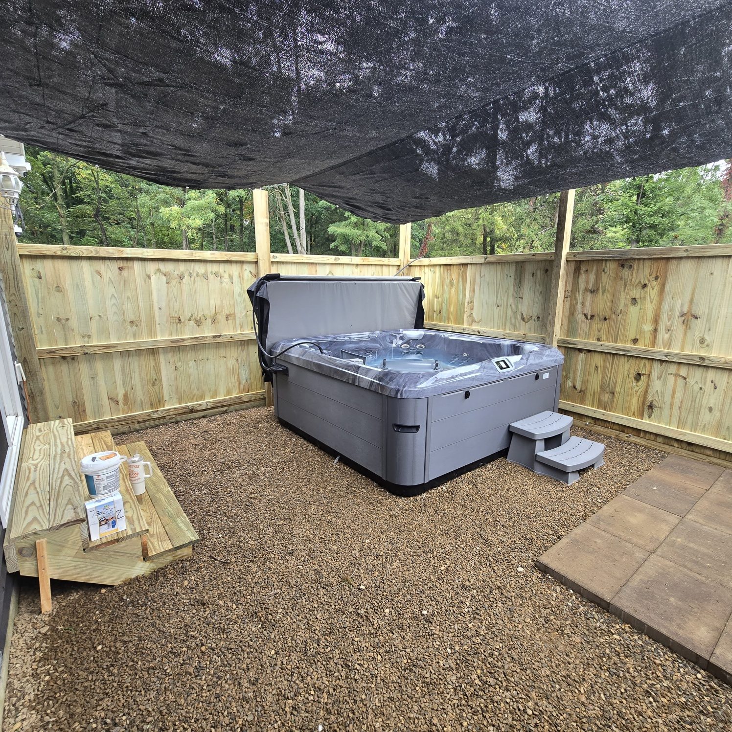Hot tub inside a new wood privacy fence with a shade sail overhead in Southwest Michigan