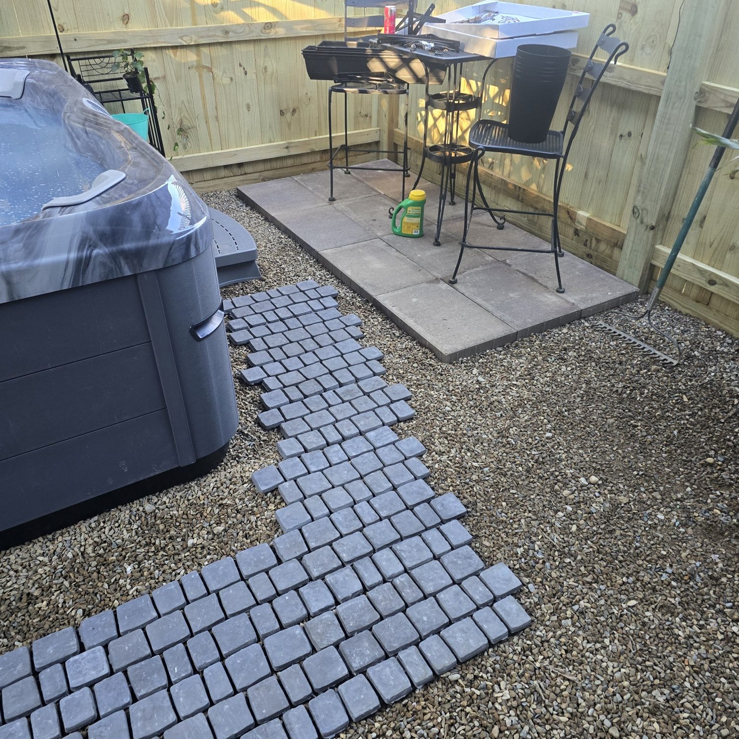 Gray cobblestone pavers being laid beside a hot tub for a backyard patio in Southwest Michigan