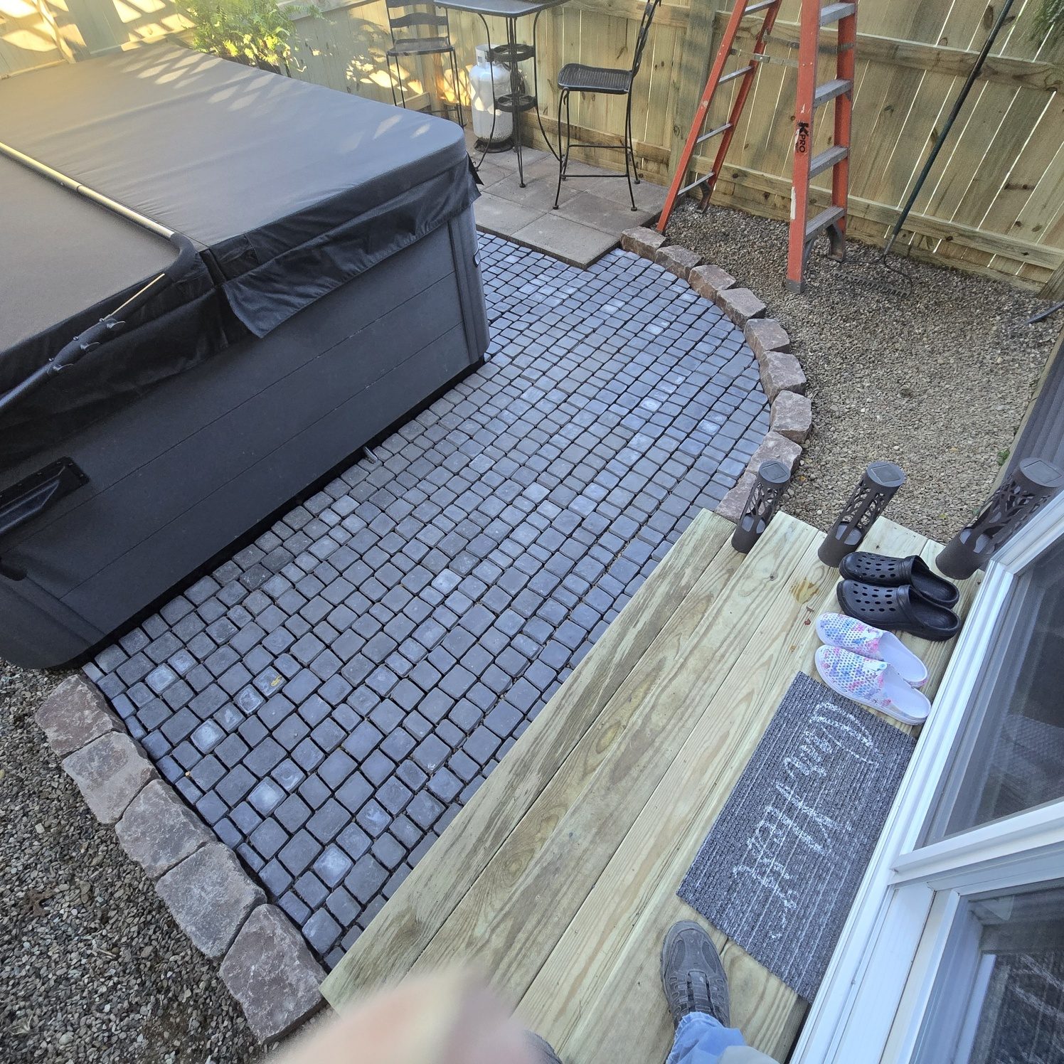 Curved gray paver patio with stone edging and new wooden steps at the back door in Southwest Michigan
