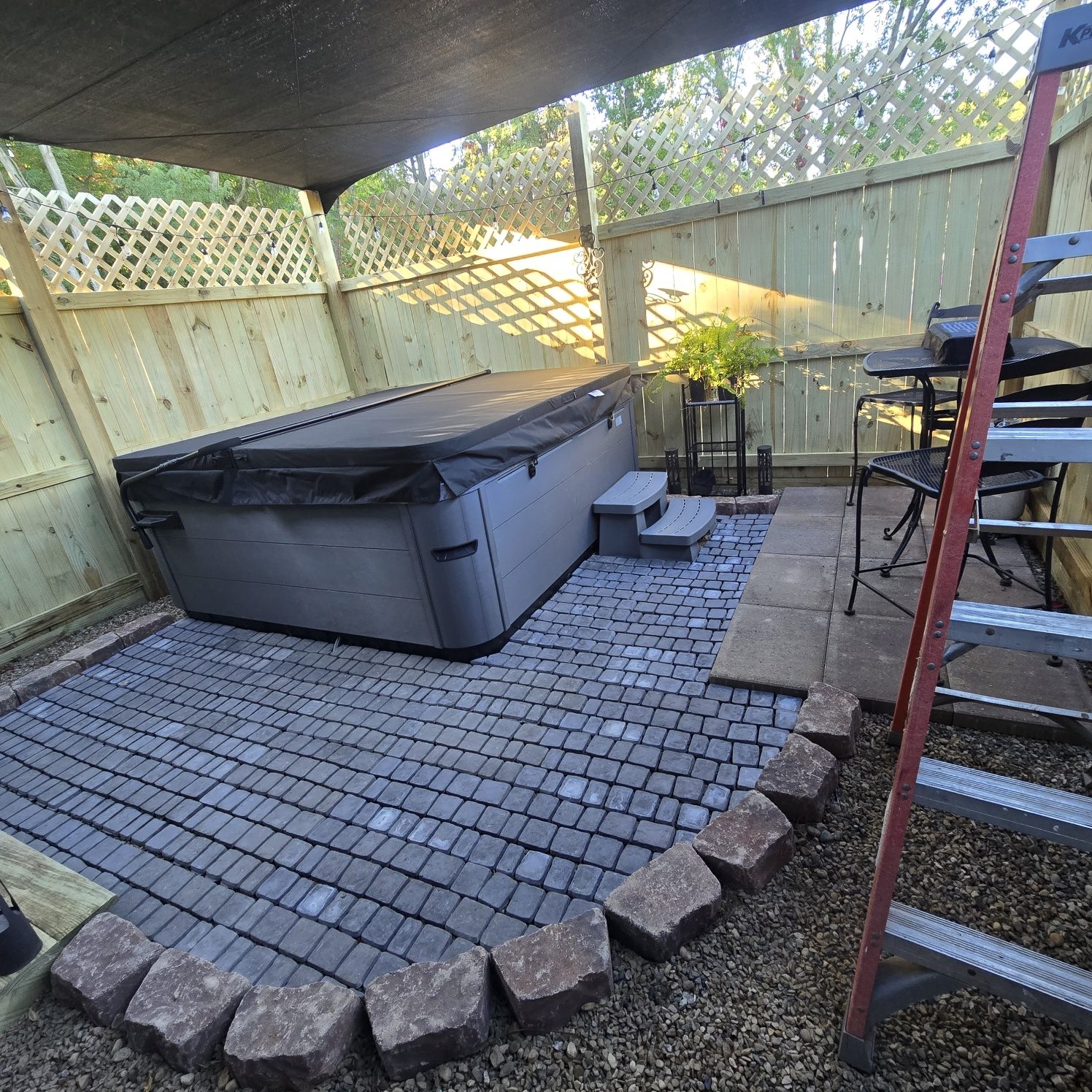 Curved paver patio with tumbled stone edging wrapping a hot tub in a fenced backyard in Southwest Michigan