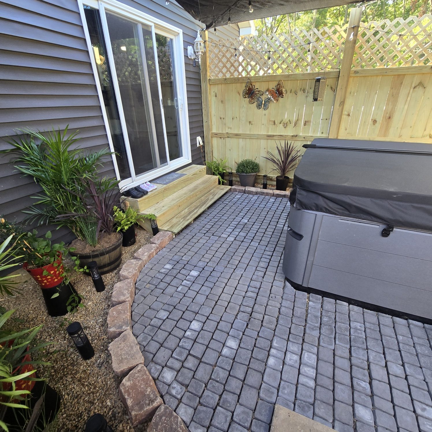 Finished paver patio with wooden steps up to a sliding door beside a hot tub in Southwest Michigan