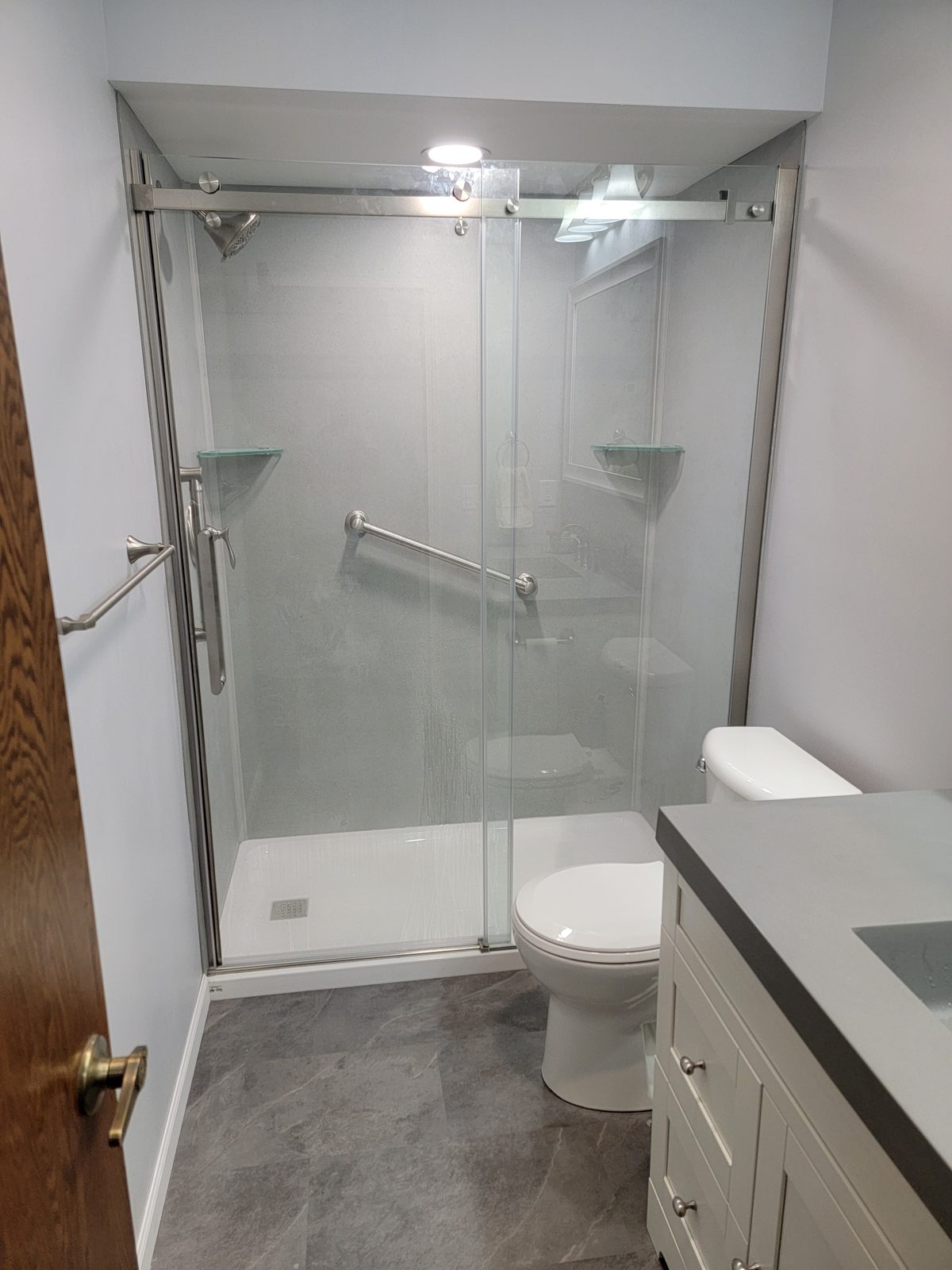 Finished basement bathroom shower with glass sliding doors, grab bar and corner shelves in Southwest Michigan