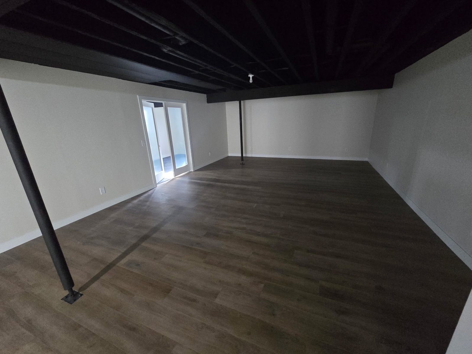Finished basement rec room in Plainwell, MI with wood-look vinyl plank flooring, white walls and black exposed ceiling