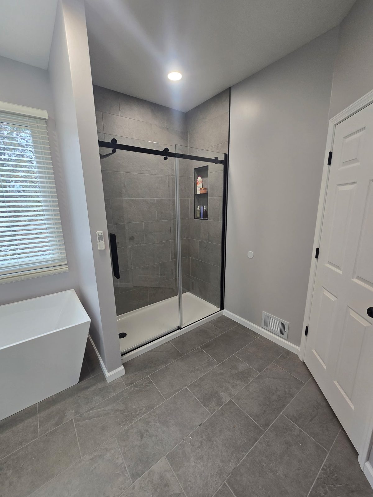 Finished walk-in tile shower with recessed niche and matte-black glass door hardware — bathroom remodel in Plainwell, MI