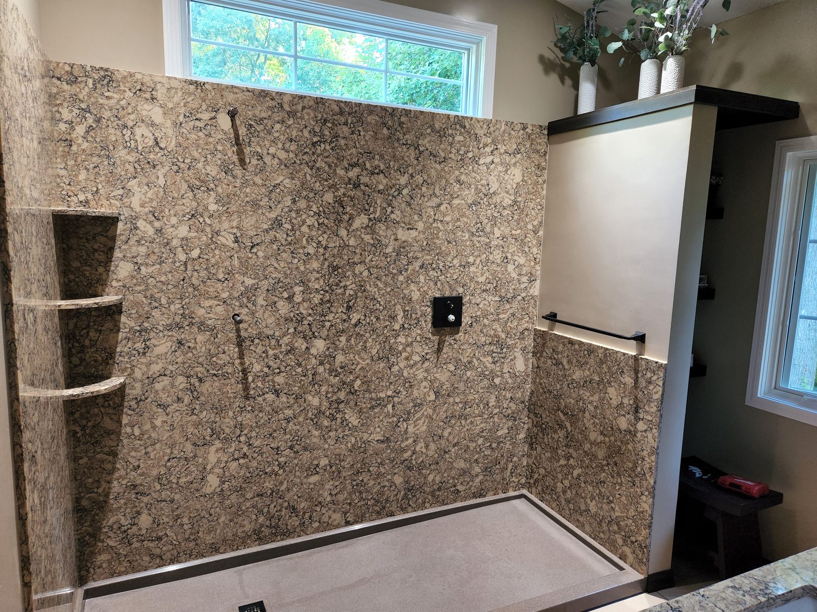 Finished walk in shower with granite look wall panels, corner shelves and black fixtures in Southwest Michigan