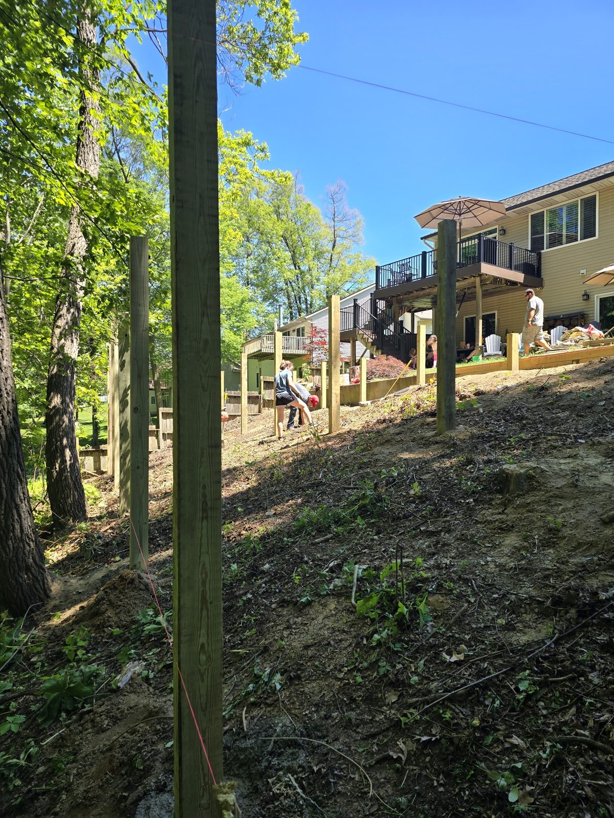 Posts set along a steep wooded slope during a retaining wall and deck project in Southwest Michigan