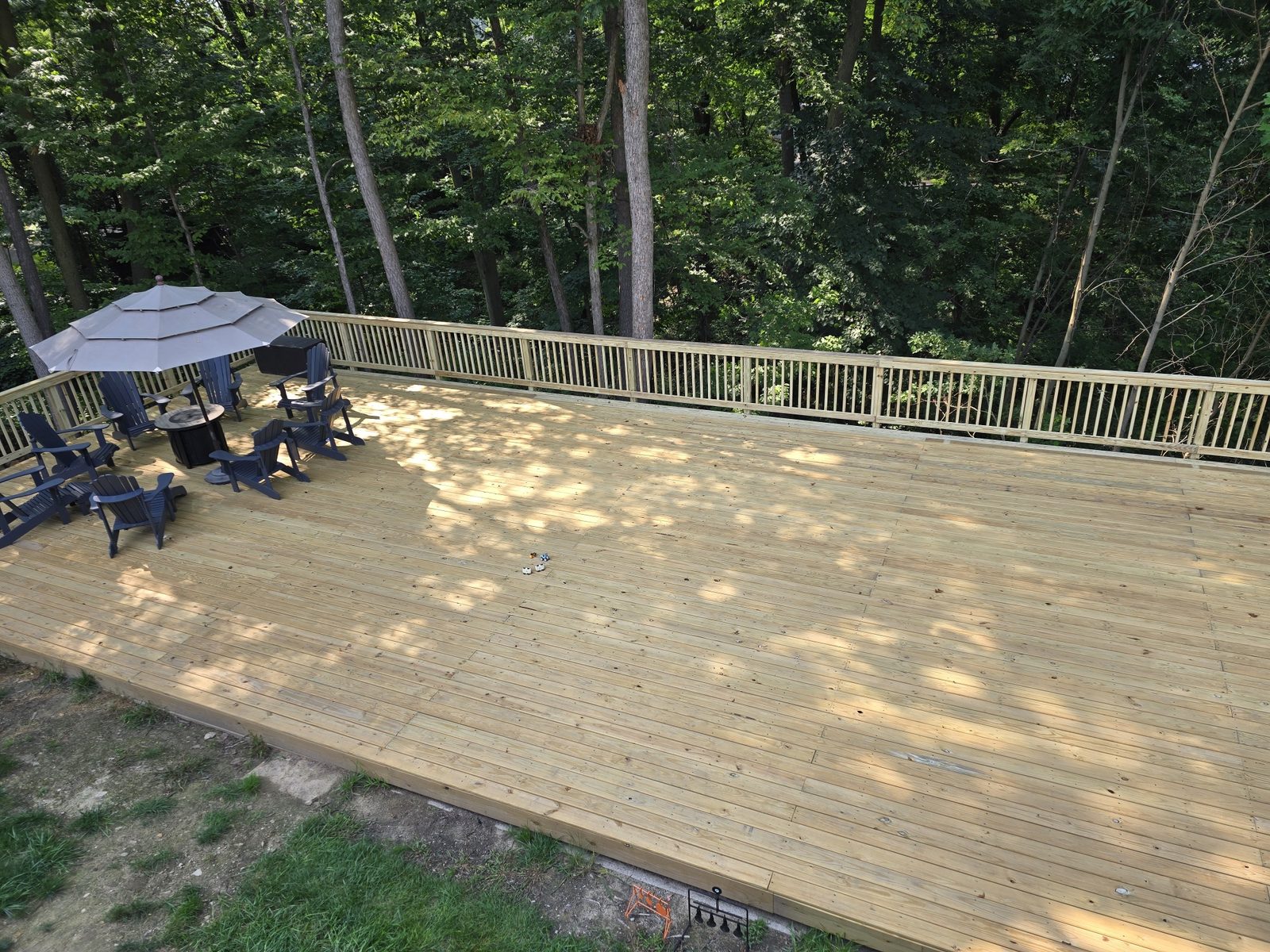Finished large backyard deck with wood railings and patio furniture under the trees in Southwest Michigan