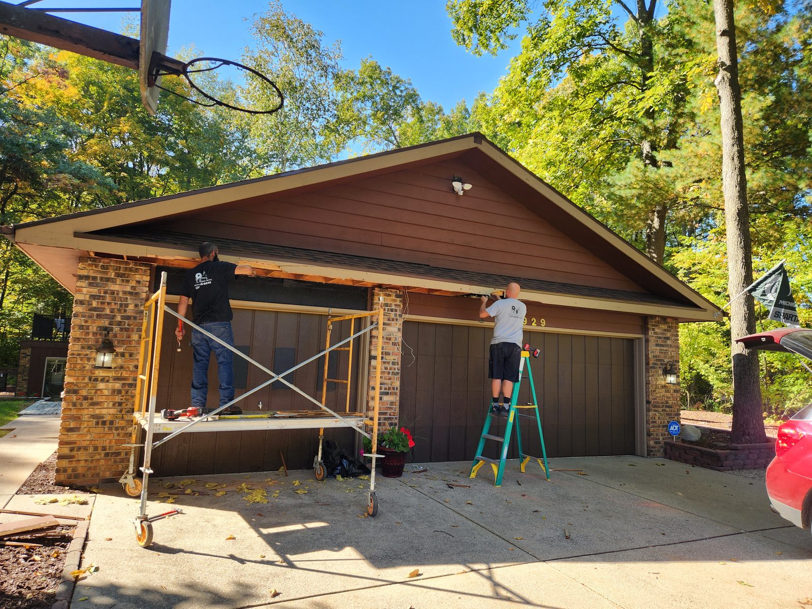 Quality Finish crew on scaffolding repairing the garage roofline of a brick and wood sided home in Southwest Michigan