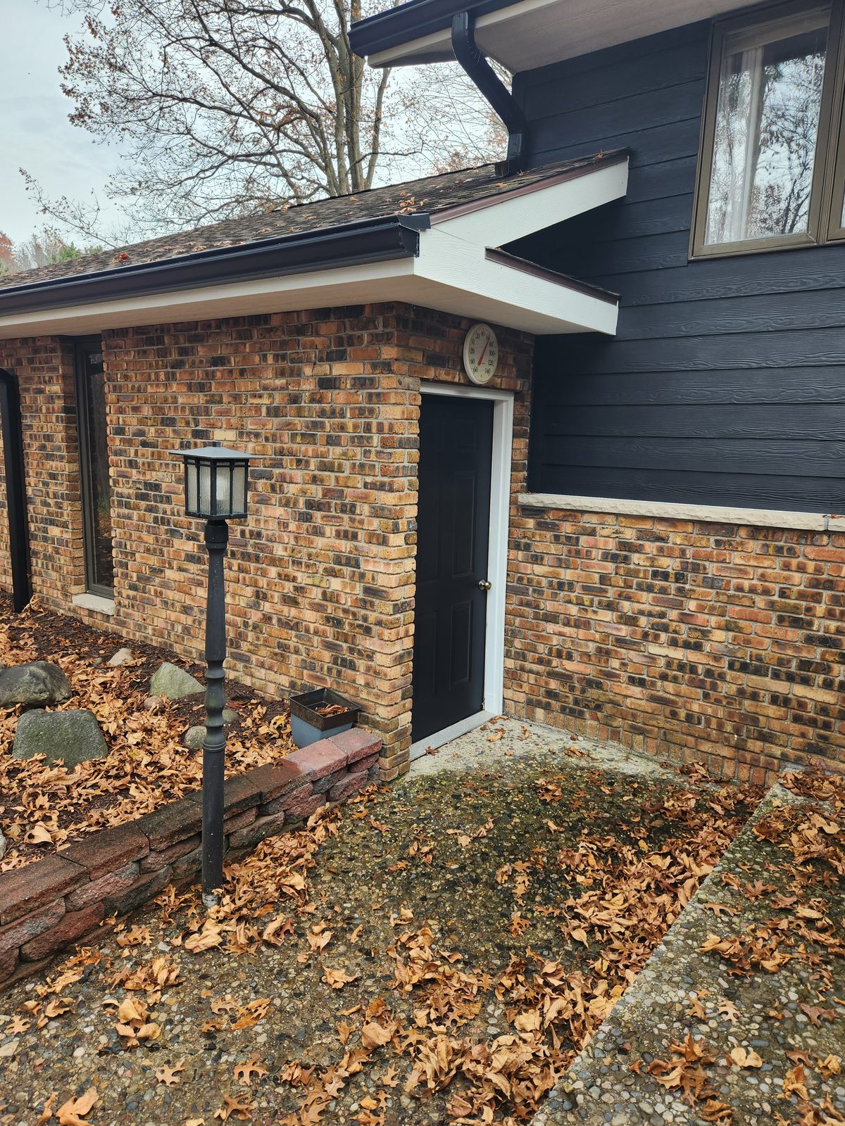 Side entry of a brick home in Southwest Michigan after roofline repair, with navy siding and crisp white trim